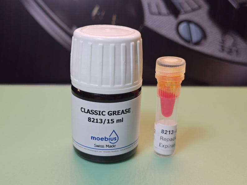 May include: A bottle of Classic Grease 8213/15 ml with a white cap and a small vial containing a pink liquid. The bottle has a black base and white label with the brand name "moebius" and "Swiss Made".