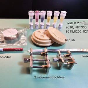 May include: A collection of watch repair tools, including a Bergeon oiler, tweezers, two movement holders, an oil dish, and six vials of oil. Also included is a piece of pithwood. The tools are arranged on a green surface.