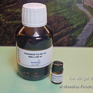 May include: Two bottles of Fixodrop ES/BS-10, one large and one small. The larger bottle has a white cap and a label with the text "FIXODROP ES/BS-10 8981/100 ml" and "moebius Swiss Made". The smaller bottle is labeled "Fixodrop 8981".