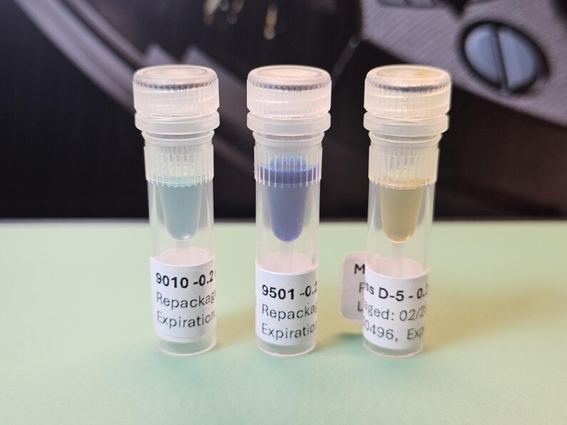 May include: Three clear vials with white caps, each containing a different colored liquid: light blue, dark blue, and yellow. Each vial has a white label with text including "Repackaged" and "Expiration".