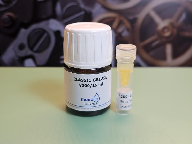 May include: A small, dark glass bottle with a white cap labeled "CLASSIC GREASE 8200/15 ml" and a smaller clear vial containing a yellow liquid. The bottle has a blue logo and the words "moebius Swiss Made".