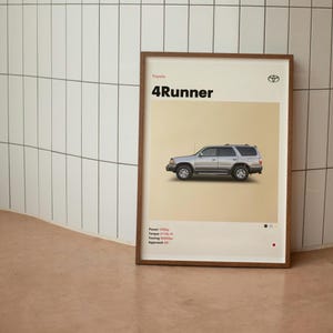 Könnte beinhalten: Gerahmter Druck mit einem silbernen Toyota 4Runner SUV. Der Druck hat einen beigefarbenen Hintergrund mit dem Text "4Runner" in Schwarz. Der Druck enthält auch das Toyota-Logo und Fahrzeugspezifikationen.