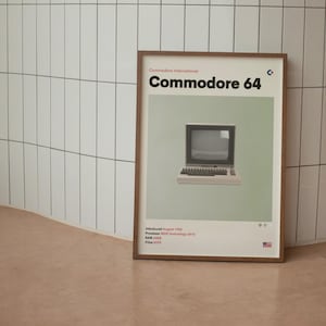May include: Framed poster featuring a vintage Commodore 64 computer. The poster has a light green background with the computer centered. Text includes "Commodore 64" and technical specifications. The frame is a dark brown color.