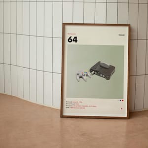 Puede incluir: Un póster enmarcado con fondo blanco y borde verde. El póster presenta una consola y un mando de Nintendo 64 negros y grises. El texto "Nintendo 64" está en blanco y negro en la parte superior del póster. El texto "Released June 23, 1996" está en blanco y negro en la parte inferior del póster.