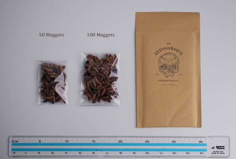 May include: Two clear plastic bags containing brown maggots, labeled "50 Maggots" and "100 Maggots". A brown paper envelope with the text "the REDmarketFX PREMIUM QUALITY" is in the background.