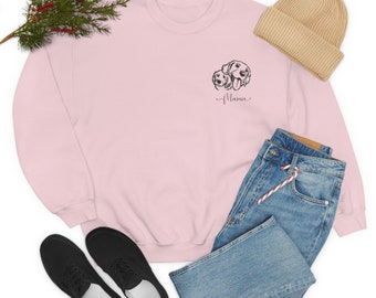 Könnte beinhalten: Ein hellrosa Sweatshirt mit einer schwarzen Grafik von zwei Hunden und dem Wort "Mama" in Schreibschrift. Das Bild enthält blaue Jeans, schwarze Schuhe und eine beige Mütze. Ein Zweig mit Grün befindet sich in der oberen linken Ecke.