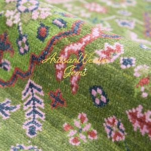 May include: Close-up of a green rug with a pink and red floral pattern. The rug has a textured surface and is woven with intricate details.