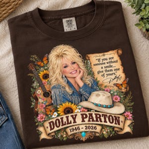 May include: A dark brown t-shirt featuring a graphic of Dolly Parton wearing a denim jacket with fringe. The design includes a guitar, sunflowers, butterflies, a cowboy hat, and a scroll with the text: If you see someone without a smile... give them one of yours. Dolly. The name Dolly Parton and the years 1946-2026 are printed on a banner at the bottom.