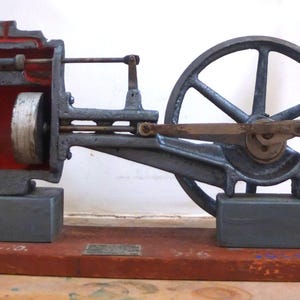 May include: A cutaway model of a steam engine with a large flywheel, a red and gray cylinder, and a wooden base.