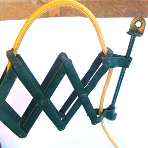 May include: A green metal folding lamp with a yellow cord. The lamp has a flexible arm that can be adjusted to different positions.