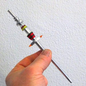 May include: A silver and red metal rocket with orange tips, held in a hand.