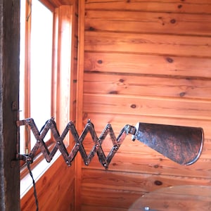 May include: A vintage-style, extendable wall lamp with a copper finish. The lamp has a flexible arm that can be adjusted to direct the light. The lamp is mounted on a wooden wall.