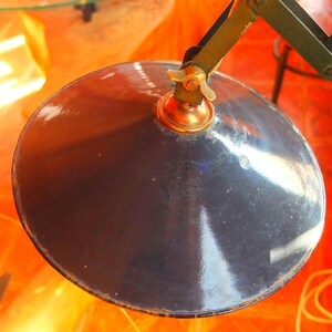 May include: A black metal lampshade with a brass fitting and a decorative knob. The lampshade is round and has a shiny finish.