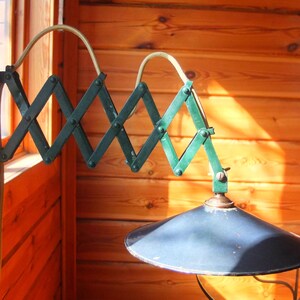 May include: A green metal wall-mounted lamp with a telescoping arm and a black metal shade. The lamp is mounted on a wooden wall.