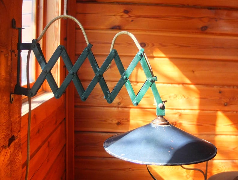 May include: A green metal wall-mounted lamp with a telescoping arm and a black metal shade. The lamp is mounted on a wooden wall.