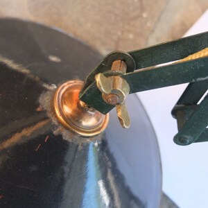May include: A vintage green metal desk lamp with a black metal shade and a brass adjustment knob. The lamp has a flexible arm and a cord.