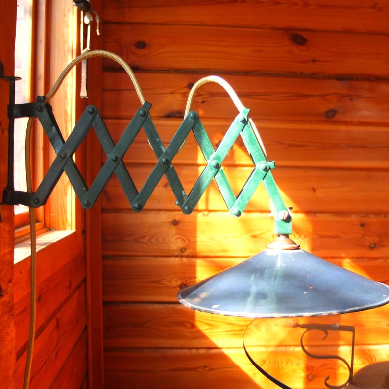 May include: A green and black metal adjustable wall lamp with a dark blue lampshade. The lamp is mounted on a wooden wall.