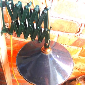 May include: A vintage green metal extendable lamp with a black metal shade. The lamp is attached to a brick wall with a yellow cord.