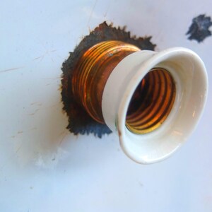 May include: Close-up of a white porcelain light socket with a copper and gold threaded base.
