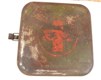 May include: A vintage, square, metal first aid kit with a rusty, distressed appearance. The kit is olive green with a red cross emblem in the center. A metal clasp and hinge are visible on the side. The overall aesthetic suggests a well-used, antique item.
