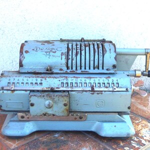 May include: A vintage blue metal adding machine with a rusty exterior. The machine has a display with numbers and a lever on the side. The machine is labeled "Феликс М".