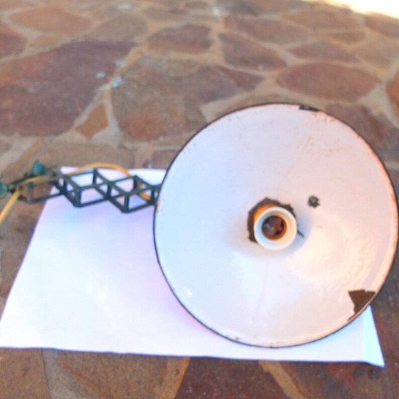 May include: A white metal lampshade with a black rim and a yellow light bulb socket. The lampshade is attached to a black metal frame with a series of square shapes.