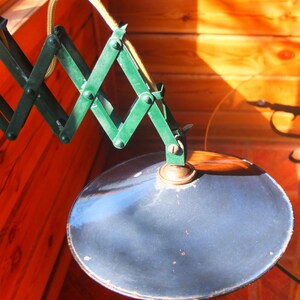 May include: A vintage green metal lamp with a flexible arm and a blue metal shade. The lamp is attached to a wall or ceiling.
