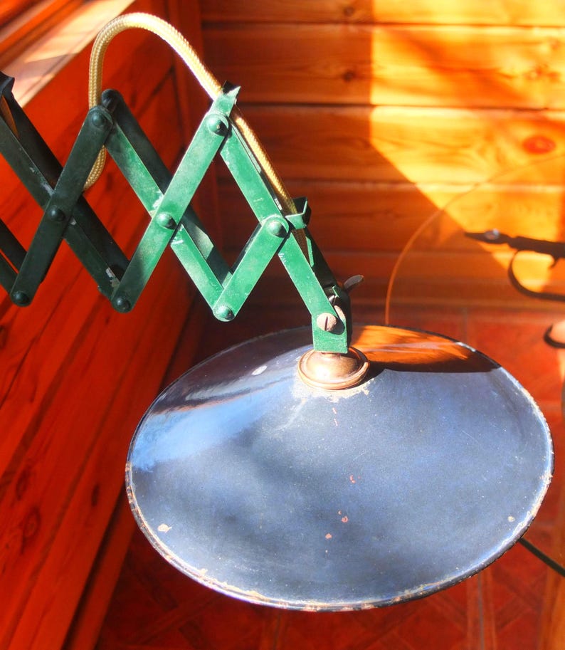 May include: A vintage green metal lamp with a flexible arm and a blue metal shade. The lamp is attached to a wall or ceiling.