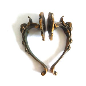 Può includere: Maniglie antiche in bronzo con design curvi e ornati. Le maniglie presentano un rilievo dettagliato di un volto e accenti floreali. Il bronzo ha una finitura patinata con sfumature di verde e oro, che aggiungono all'estetica vintage.