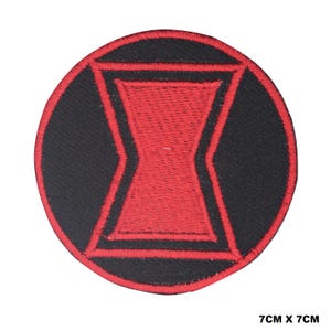 May include: A circular embroidered patch featuring a black background with a red hourglass symbol in the centre, surrounded by a red border. The patch measures 7 cm by 7 cm as indicated by the text printed in the bottom right corner of the image.
