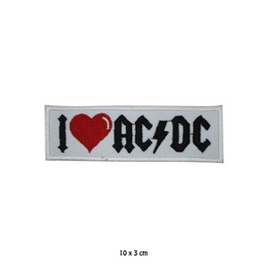 May include: A rectangular embroidered patch with a white background featuring the text I, a red heart, and the text AC/DC in black with a lightning bolt symbol. The patch measures 10 x 3 cm as indicated by the text printed below the item.