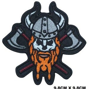 Peut inclure: Un écusson brodé mesurant 9,8 cm sur 9,8 cm représentant une tête de Viking avec un casque à cornes, une barbe orange épaisse et deux haches de combat croisées derrière la tête. Le motif est souligné par un fil noir avec des détails gris et orange.
