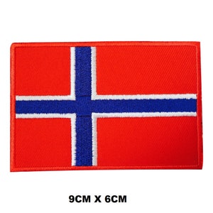 May include: An embroidered patch of the Norwegian flag, featuring red, white and blue colours. The patch measures 9 cm by 6 cm.