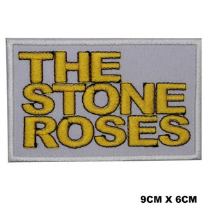 Może przedstawiać: Żółta naszywka haftowana z tekstem "THE STONE ROSES" na szarym tle. Naszywka ma wymiary 9 cm x 6 cm.