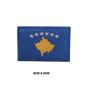 May include: Embroidered patch of the Kosovo flag. The flag is blue with a yellow outline of the country's map in the center and six white stars in a semi-circle above the map. The patch measures 9 cm by 6 cm.