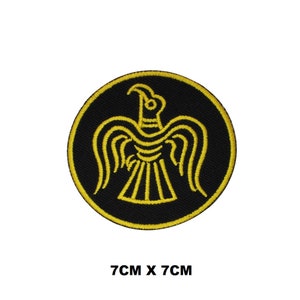 Könnte beinhalten: Ein gestickter schwarzer und gelber Aufnäher mit einem stilisierten Vogelmotiv. Der Aufnäher ist rund und hat einen Durchmesser von 7 cm.