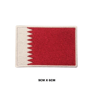 Puede incluir: Un parche bordado de la bandera de Qatar. La bandera es roja con un triángulo blanco dentado en el lado del asta. El parche mide 9 cm por 6 cm.