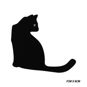 Può includere: Toppa con silhouette di gatto nero, misura 7 cm x 8 cm. Il gatto è raffigurato in posizione seduta con la coda estesa. La toppa ha un dettaglio dell'occhio bianco ed è su sfondo bianco.
