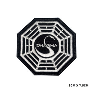 Puede incluir: Parche bordado en blanco y negro con el logotipo de la Iniciativa Dharma. El logotipo es un octógono con un cisne estilizado en su interior, y la palabra "DHARMA" escrita debajo del cisne.