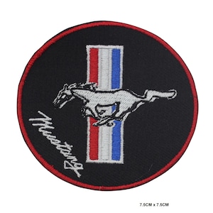 May include: A circular black patch with a red border, displaying the Mustang logo. The logo features a white running horse, a vertical stripe in red, white, and blue, and the word "Mustang" in white script. The patch measures 7.5cm x 7.5cm.
