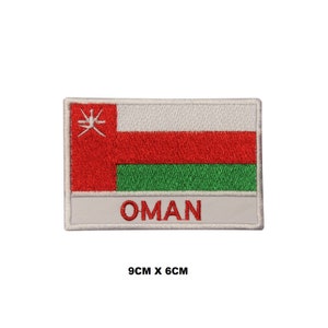 Pode incluir: Um remendo bordado com a bandeira de Omã. A bandeira é vermelha, branca e verde com uma borda vermelha e a palavra "OMÃ" escrita em vermelho abaixo da bandeira. O remendo mede 9 cm por 6 cm.