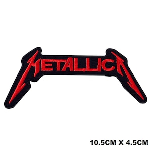 May include: An embroidered patch featuring the word METALLICA in red thread on a black background. The letters M and A have elongated, pointed strokes extending downwards. The patch measures 10.5 cm by 4.5 cm as indicated by the text.