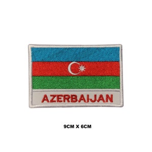 May include: Embroidered patch featuring the flag of Azerbaijan. The flag is blue, red, and green with a white crescent moon and star in the center. The patch is 9 inches by 6 inches and has the word "AZERBAIJAN" written below the flag.