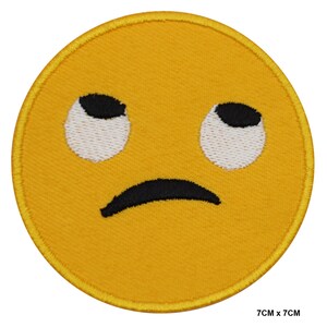 以下が含まれることがあります： 黄色い刺繍のアイロン接着パッチで、退屈または無関心な表情の漫画の顔をしています。顔は黒い眉毛、黒い瞳、白い目玉、黒いしかめっ面をしています。