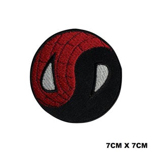 May include: A circular embroidered patch measuring 7cm by 7cm featuring a split design. One half is red with a black web pattern, and the other half is solid black. Two white, almond-shaped eye outlines are positioned within the design.