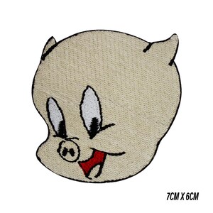May include: A beige embroidered patch featuring a cartoon pig face with black outlines, black eyes, and a red tongue. The patch measures 7cm x 6cm.