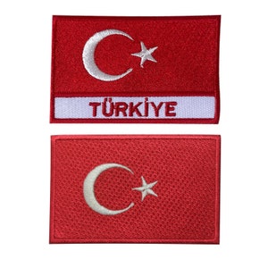 Puede incluir: Dos parches bordados rojos con la bandera turca. El parche superior incluye la palabra "TÜRKIYE" en letras blancas sobre un fondo blanco. Cada parche tiene una luna creciente y una estrella blancas.