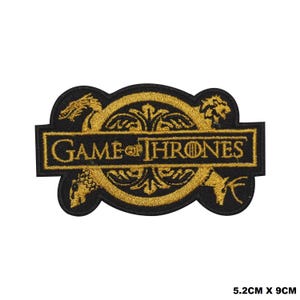 May include: A black and gold embroidered patch featuring the text GAME OF THRONES centred over a circular emblem with four animal figures. The patch measures 5.2 cm by 9 cm and displays intricate stitching of a dragon, lion, and stag.