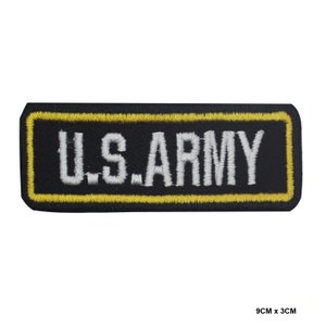 Op de afbeelding: Zwarte geborduurde patch met een gele rand en de tekst "U.S. ARMY" in witte letters. De patch is 9 cm bij 3 cm.