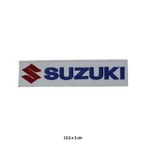 Könnte beinhalten: Ein rechteckiger weißer Aufnäher mit dem Wort "SUZUKI" in Blau und dem Suzuki-Logo in Rot. Der Aufnäher misst 12,5 x 3 cm. Es handelt sich wahrscheinlich um ein gesticktes Emblem.